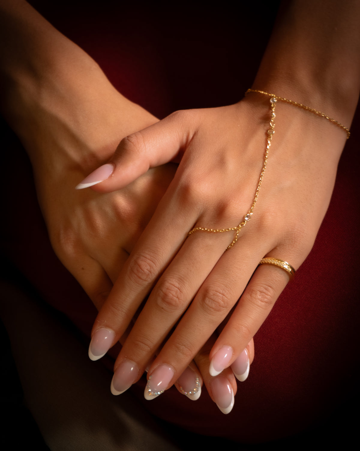 Setu gold plated hand chain with zircon stones worn on the hand, resting on a deep red background